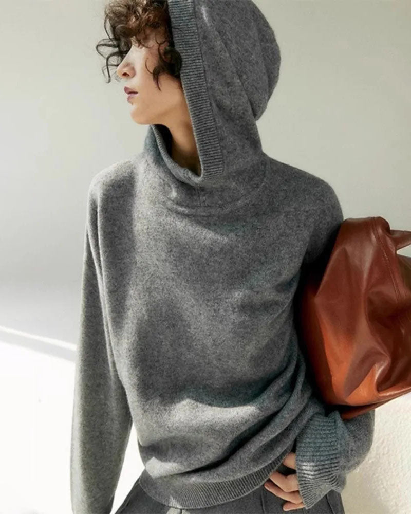 Woman lounging in the Base Knit Sweater Hoodie, recycled-polyester knit and relaxed drop-shoulders give cabin vibes—your wind-proof 55-70 °F spring-fall layer that doubles as a statement piece on campus nights.